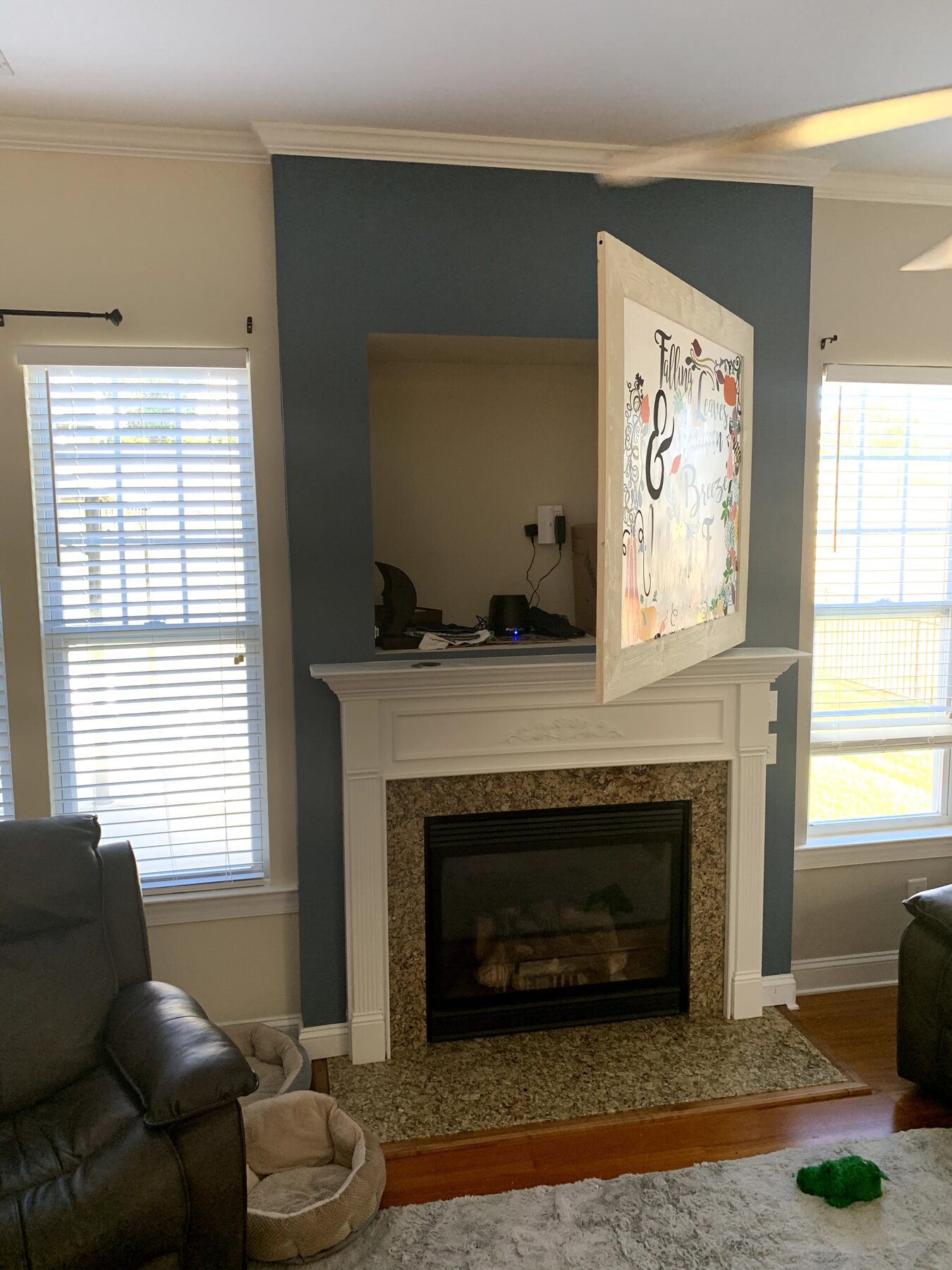 Custom hinged picture-frame cabinet door concealing a recessed media niche above a painted fireplace mantel