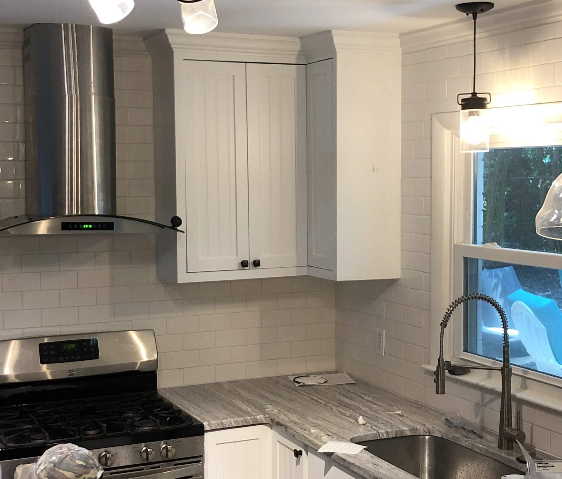 Angled corner wall cabinet over a white subway tile backsplash beside a stainless range hood and granite counter