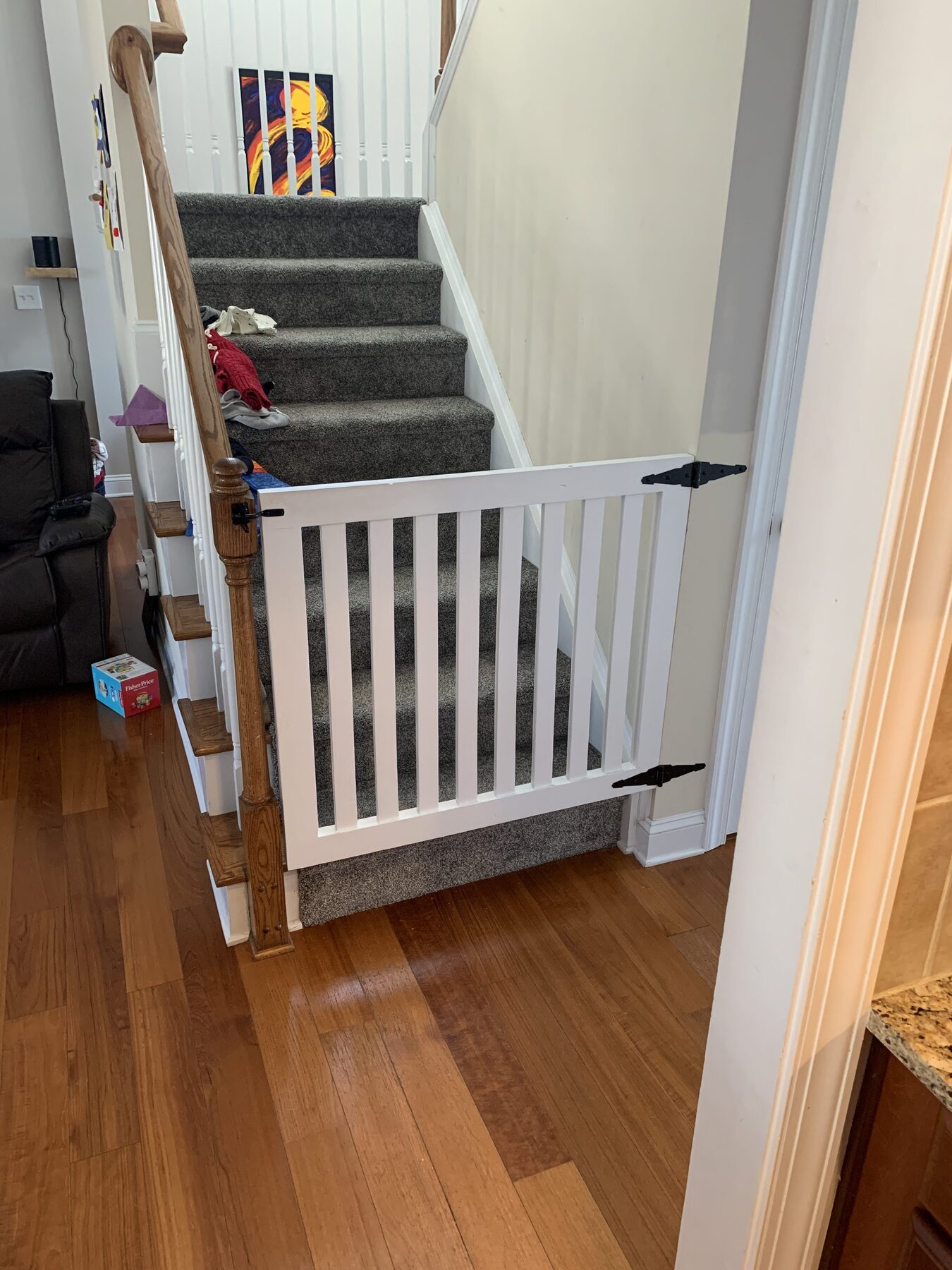 Custom white wood stair safety gate with vertical slat balusters and black strap hinges matching the staircase trim