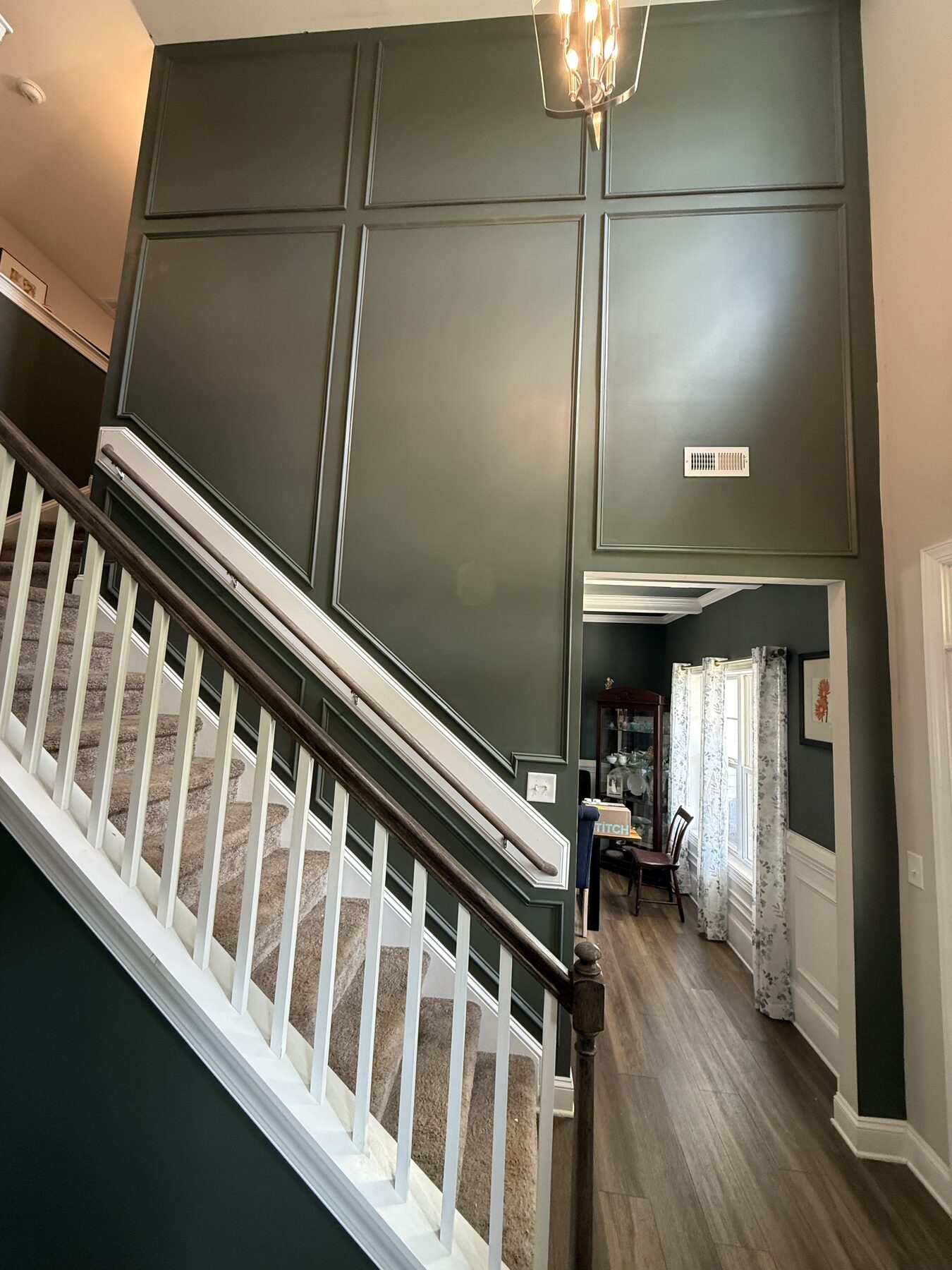 Two-story applied panel moulding accent wall in deep green rising above a stair railing and hardwood landing