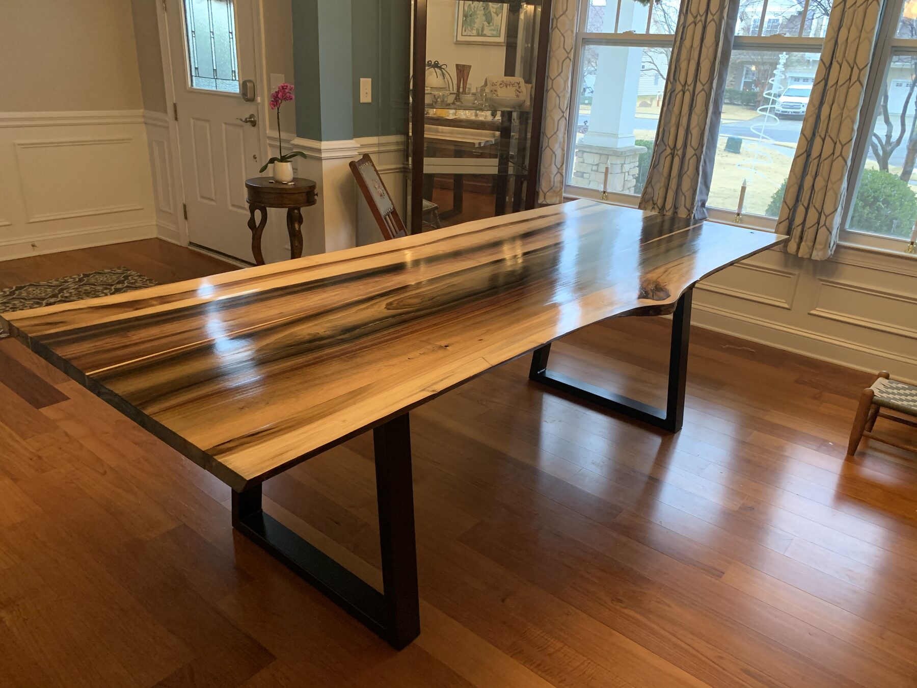 Live-edge rainbow poplar dining table with vivid green and purple grain streaks on blackened steel trapezoid legs