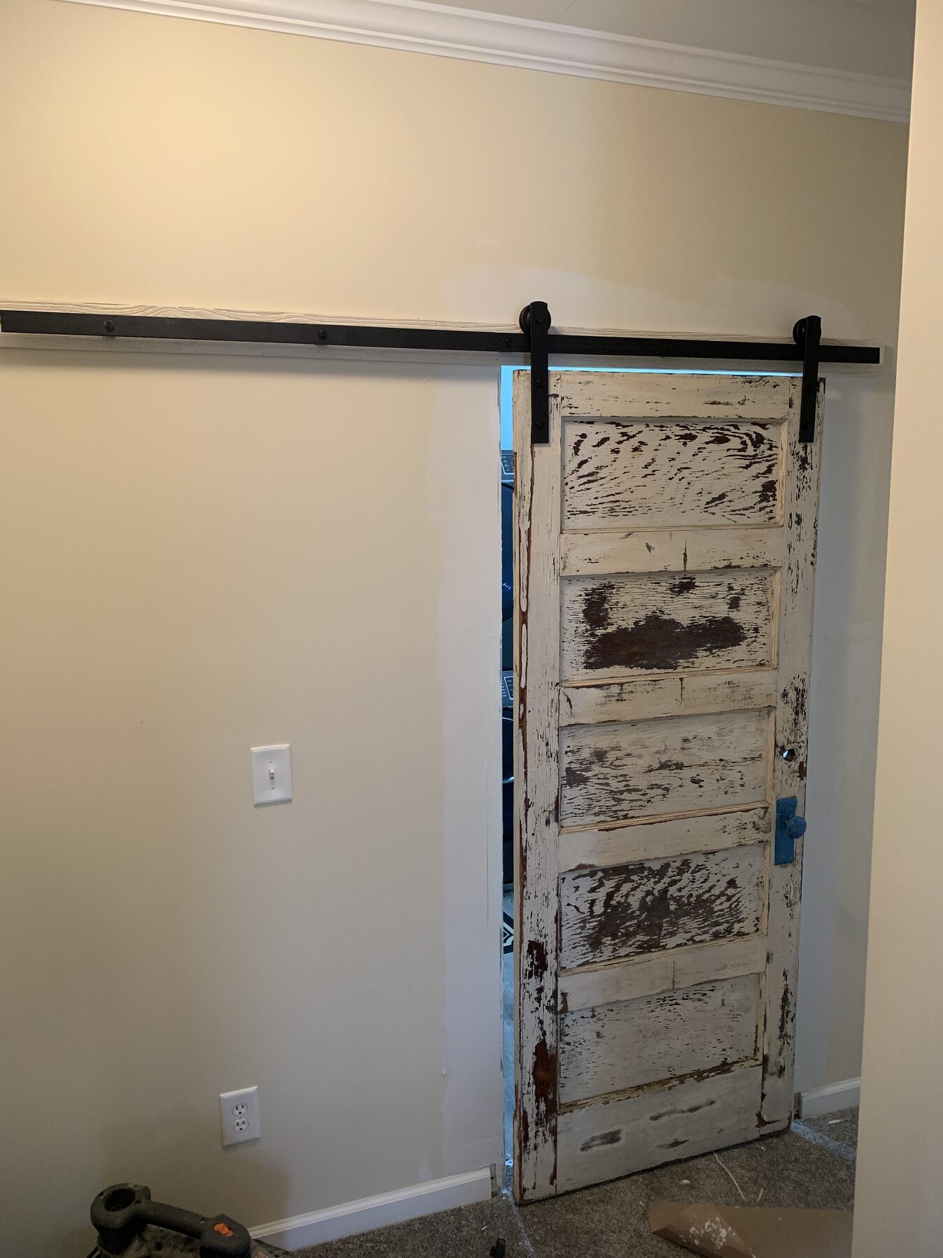 Reclaimed five-panel vintage barn door with chipped paint hung on a black rolling barn door track