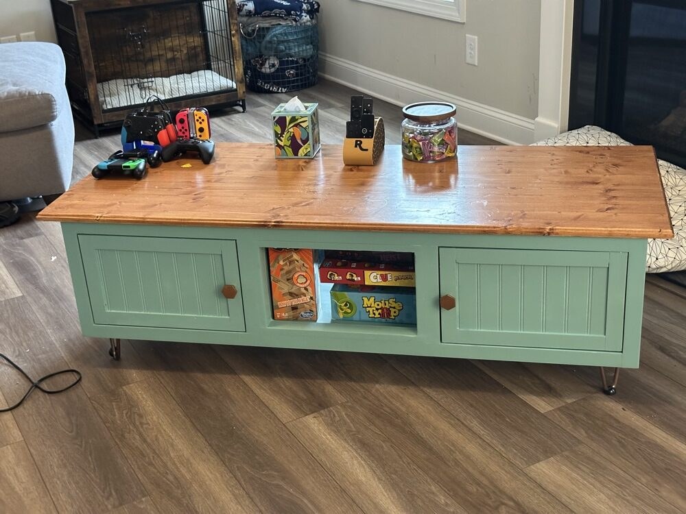 Finished seafoam green coffee table with beadboard-panel doors, open center bay and a warm stained plank top on hairpin legs