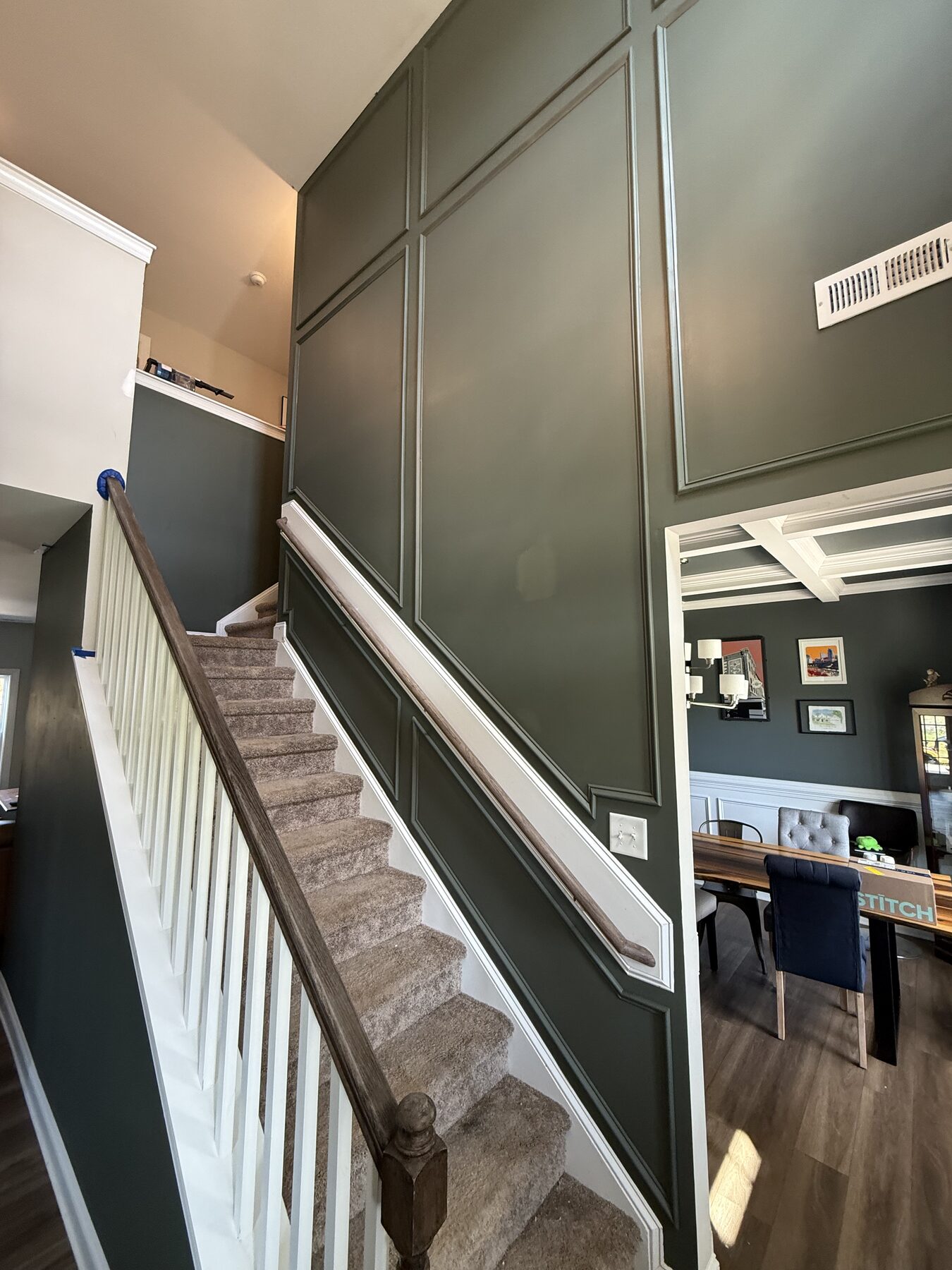 Deep green board and batten paneling running the full height of a stairwell wall beside a white balustrade