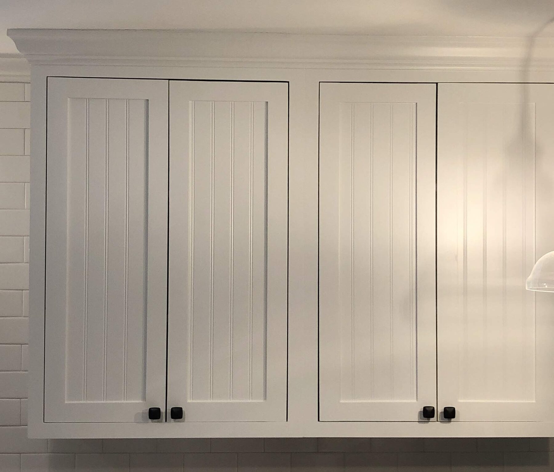 White inset beadboard-panel kitchen wall cabinets with tight reveals, stacked crown molding and matte black square knobs