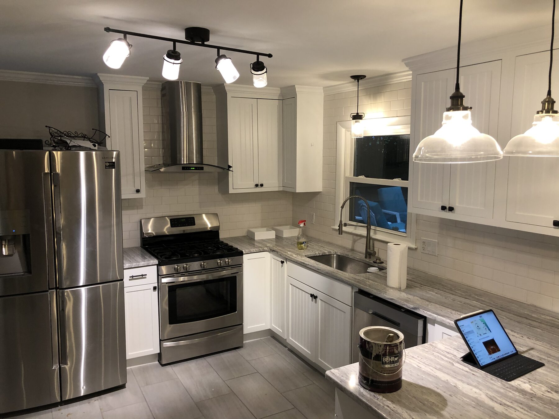 Kitchen range wall with white upper cabinets, stainless hood, tile backsplash and granite counter at the sink window